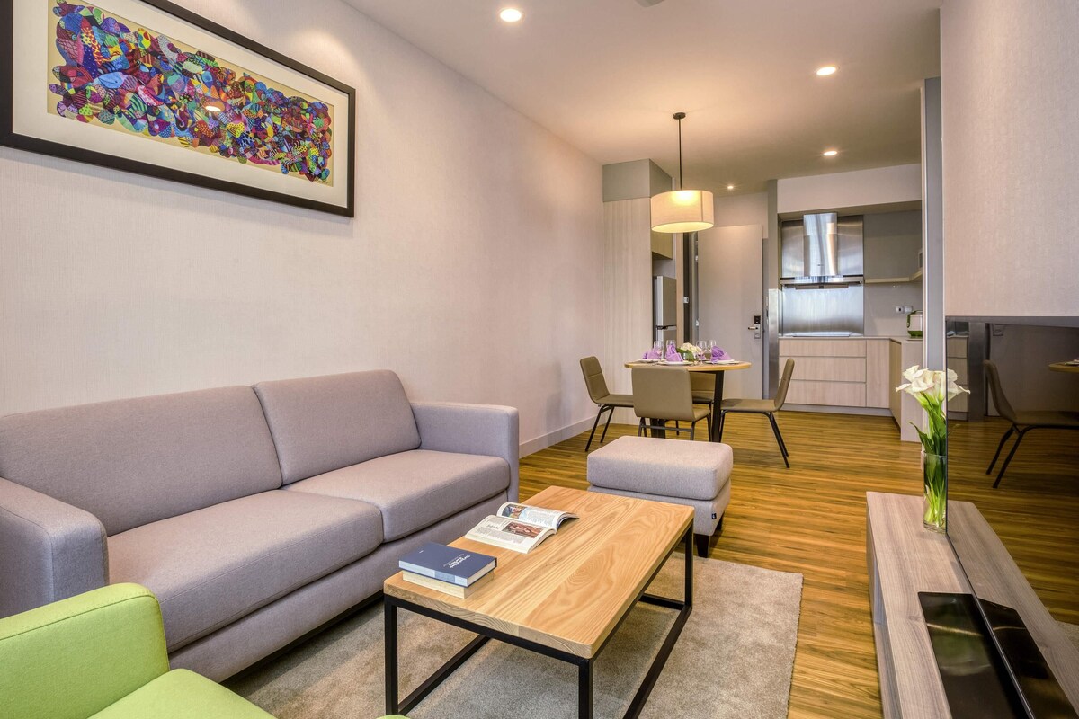 Un salon moderne avec un canapé, une table basse et un coin repas comprenant des chaises et une table dressée pour deux personnes.