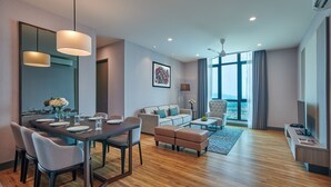 Een moderne hotelkamer met een eethoek, een bank, een televisie en een groot raam met uitzicht op de stad.