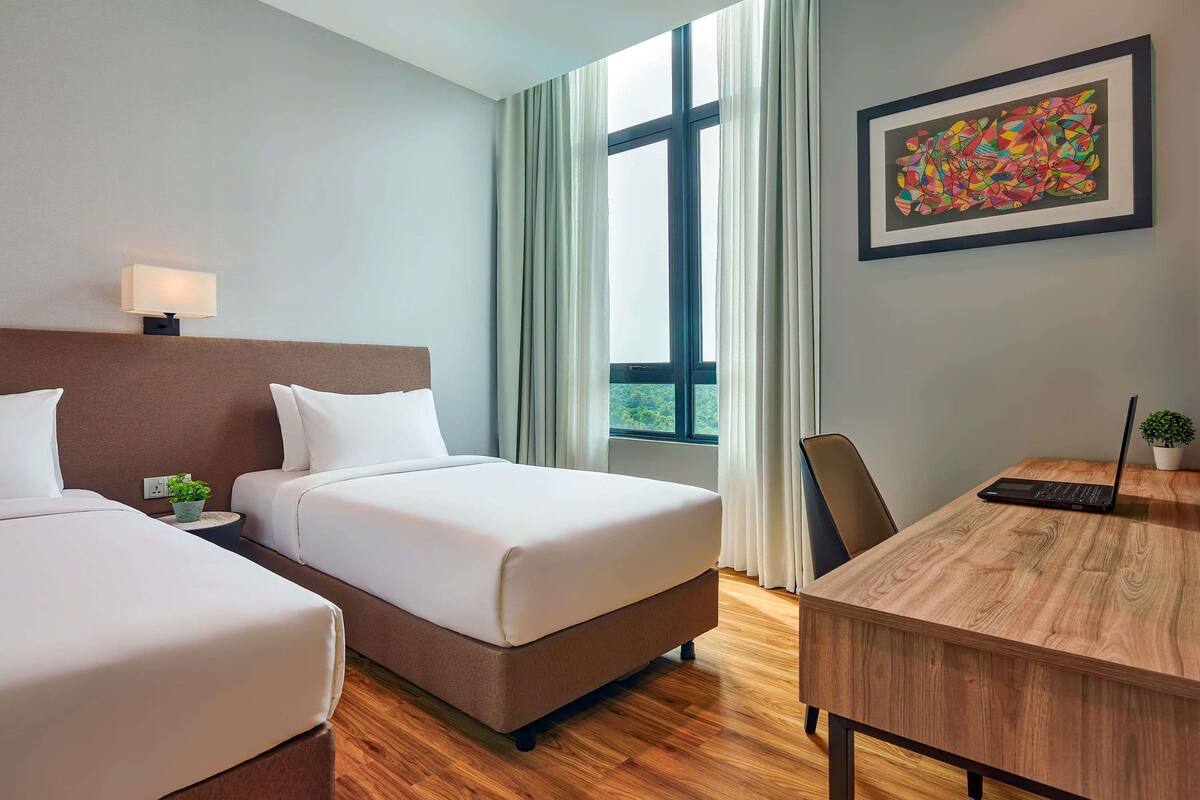 Une chambre d’hôtel avec deux lits, un bureau, un ordinateur portable, un tableau et une fenêtre avec des rideaux.