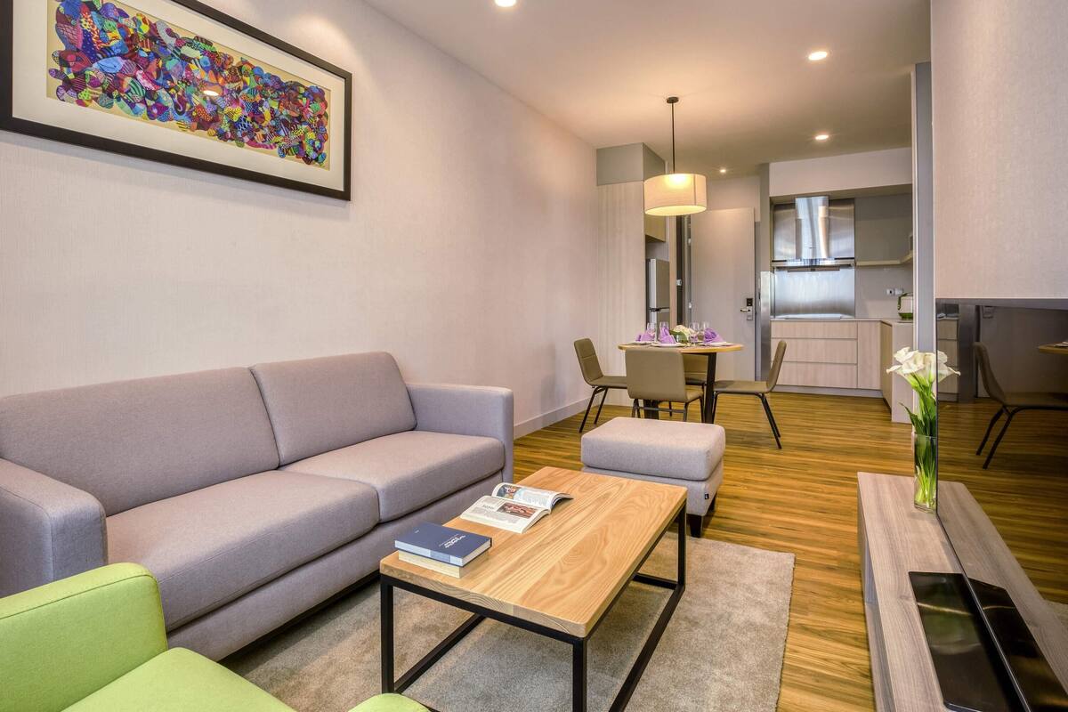 Un salon moderne avec un canapé, une table basse et un coin repas comprenant des chaises et une table dressée pour deux personnes.