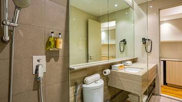 Un baño moderno con cabina de ducha de vidrio, inodoro, lavamanos con espejo y artículos de aseo en la pared.
