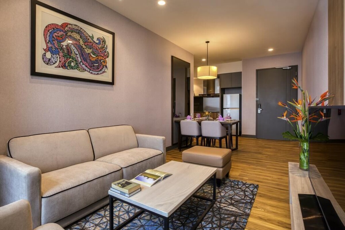 Ein modernes Wohnzimmer mit Sofa, Couchtisch und Kunstwerken. Es gibt einen Essbereich mit Stühlen und einem Tisch, sowie eine Küche im Hintergrund.