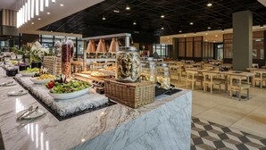 Un vaste espace de restauration intérieur doté d’un comptoir en marbre, de divers produits alimentaires et d’un plafond haut avec des poutres apparentes.