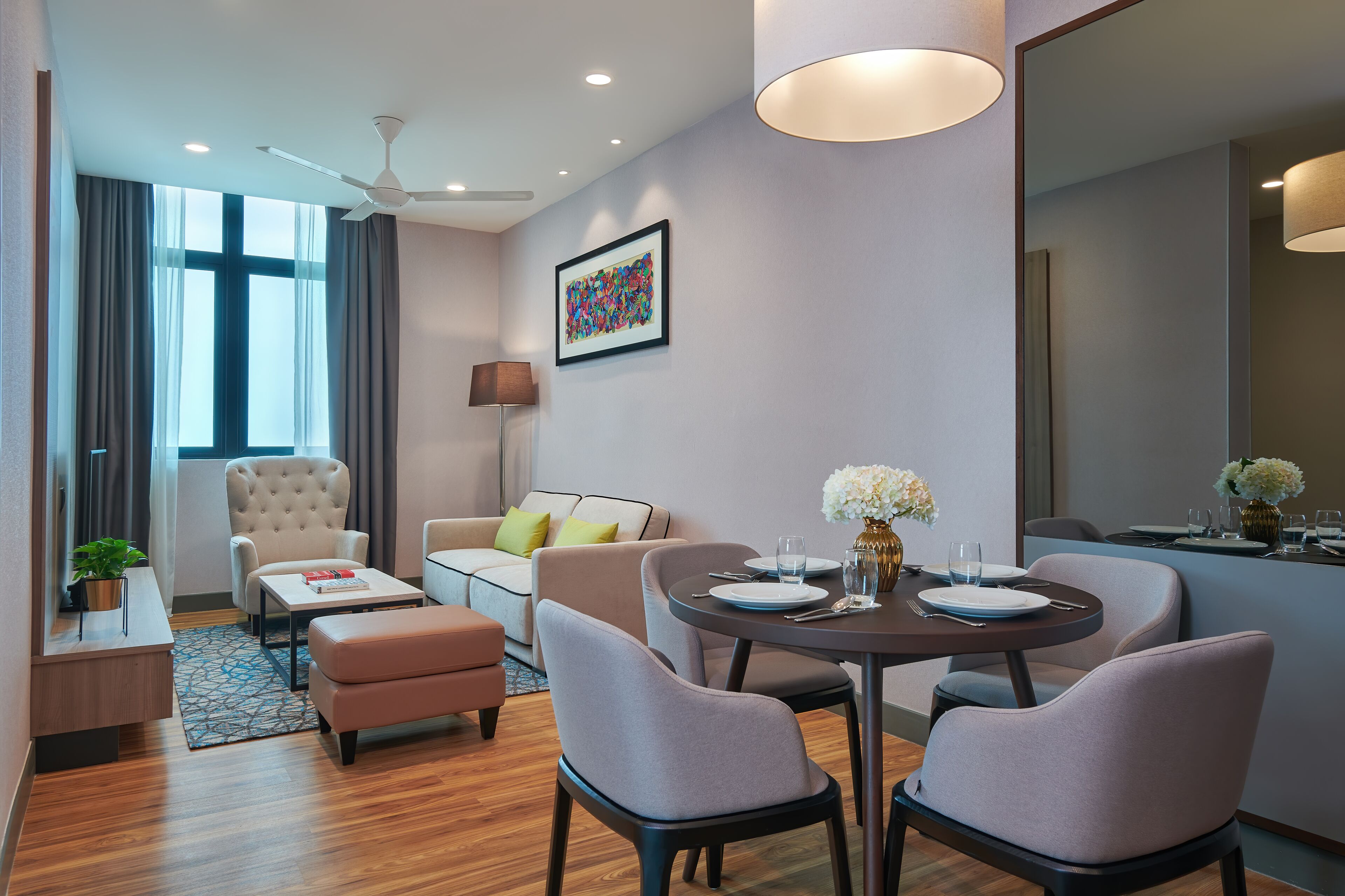 Habitación de hotel moderna con zona de comedor, sofá, sillón, mesa para dos personas y un ventanal con cortinas.
