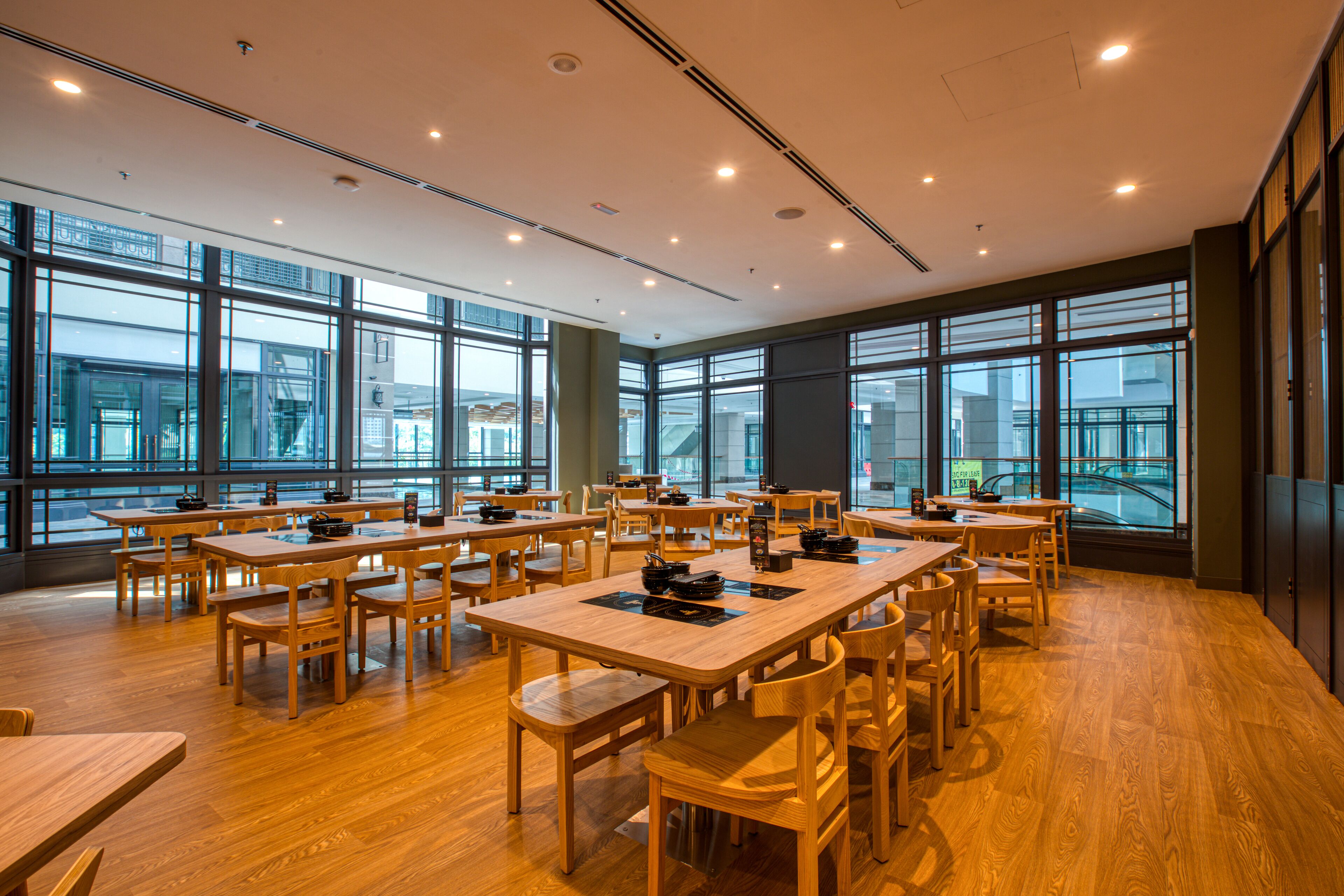 Un'ampia sala da pranzo con diversi tavoli e sedie in legno, e ampie finestre che offrono vista sulla città.
