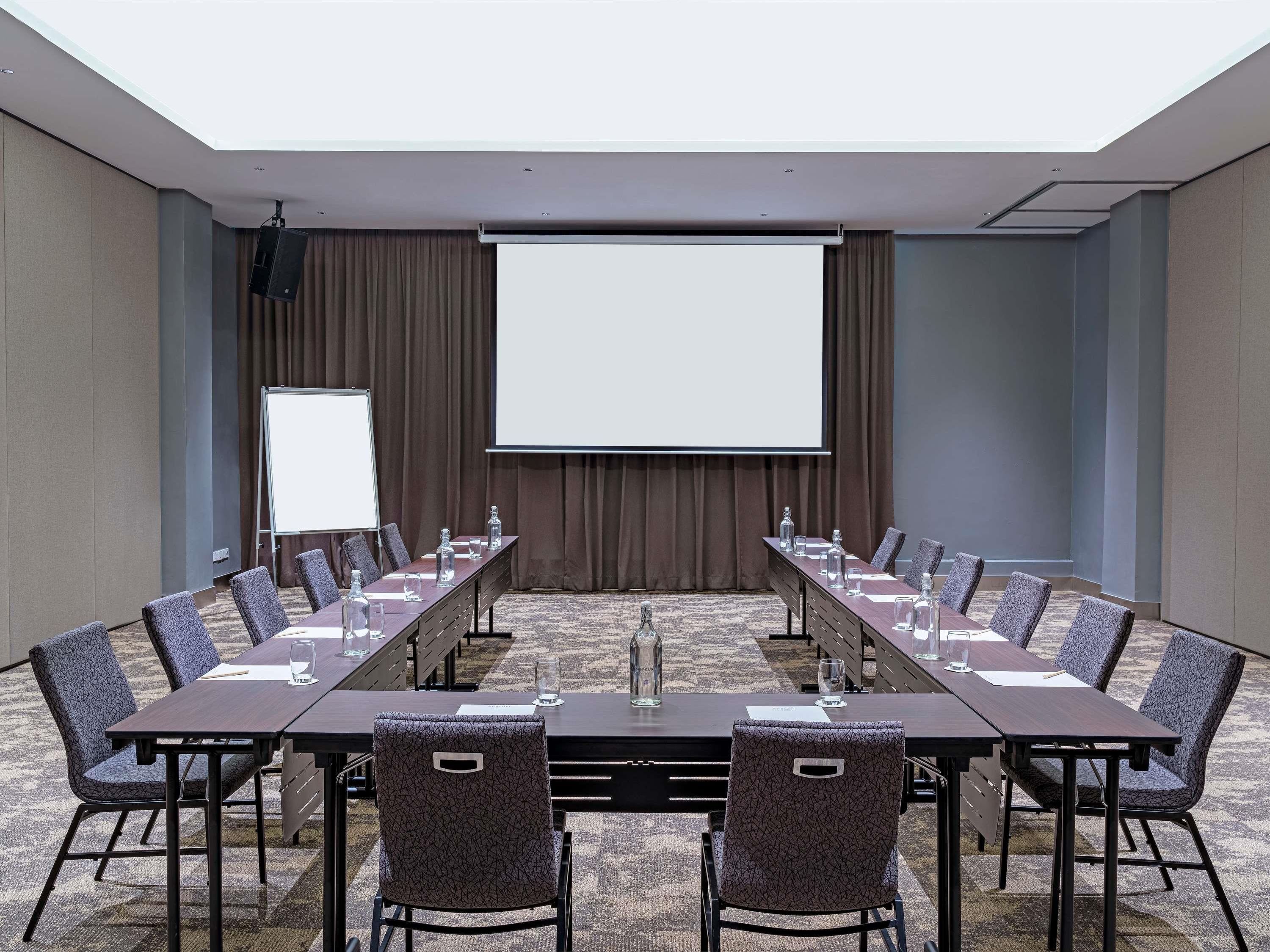 A conference room with a long table, chairs, a projector screen, and a whiteboard.