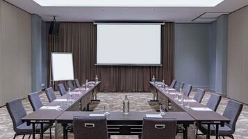 A conference room with a long table, chairs, a projector screen, and a whiteboard.