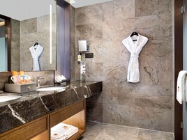 Un baño moderno con encimera de mármol, un espejo grande, una bata colgada en la pared y un perchero.