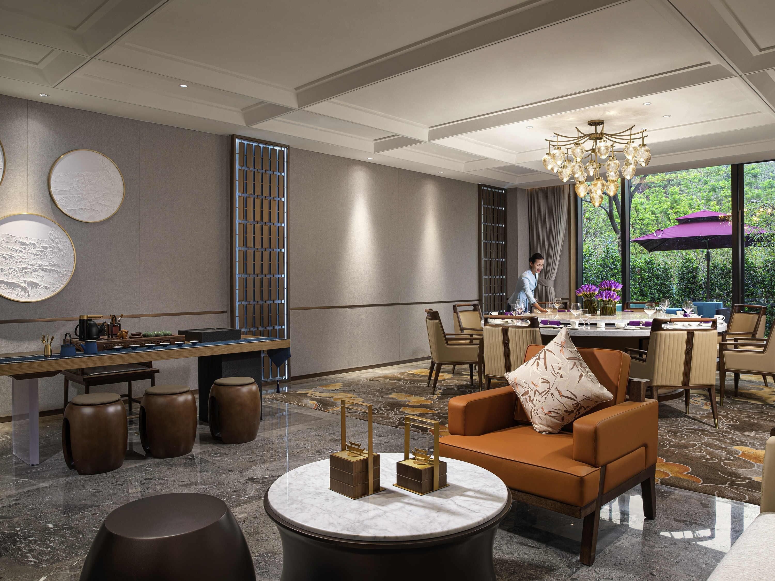 A modern dining area with a chandelier, a table set for two, and a view of greenery outside.