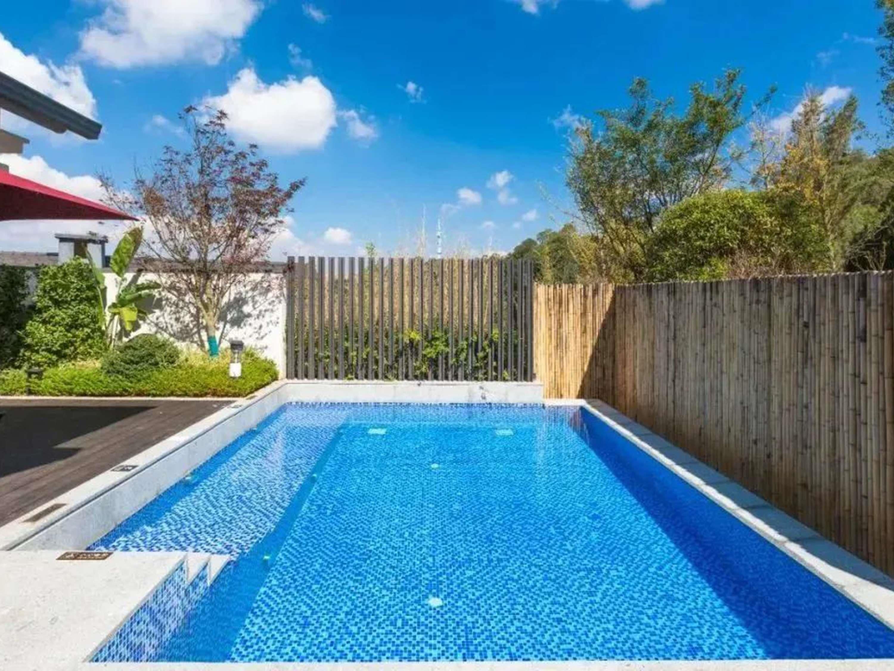 Una piscina rectangular con cercado de madera y follaje a su alrededor.