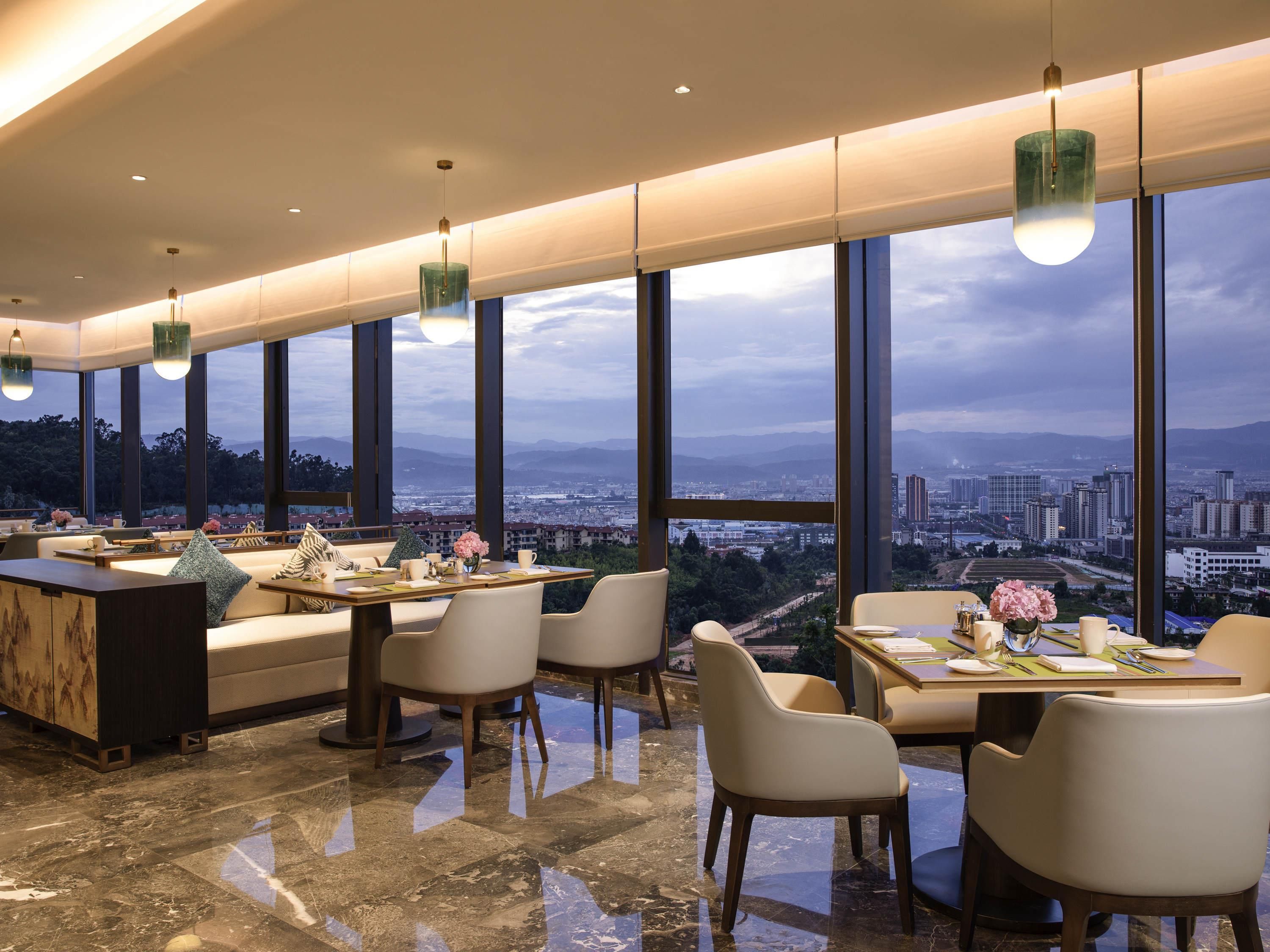 A modern dining area with large windows, a marble floor, and a city view.