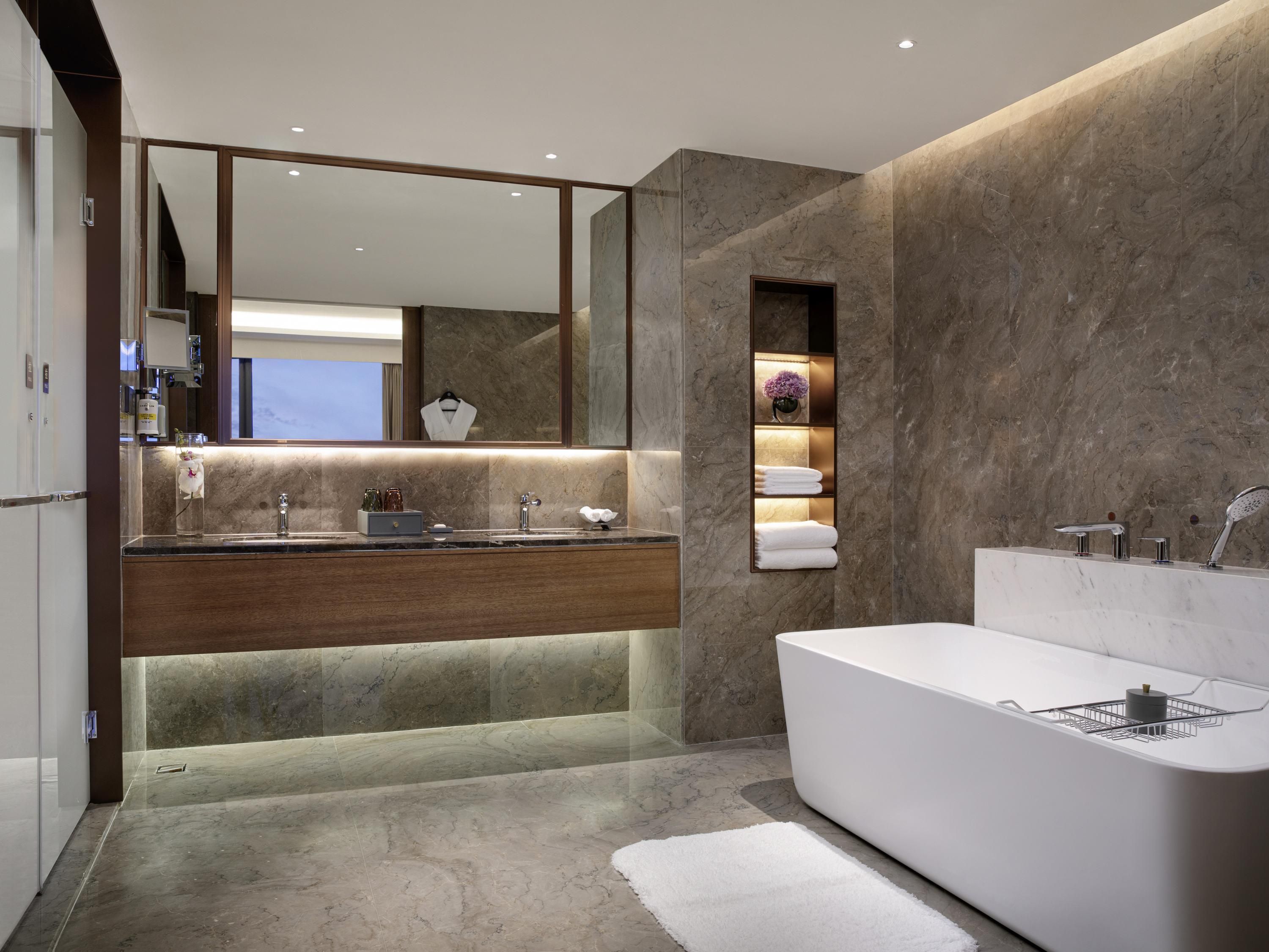 A modern bathroom with a large mirror, a built-in sink, a bathtub, and a marble wall.