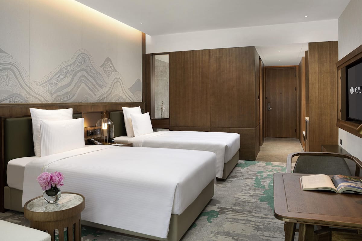A hotel room with two beds, a small table with a vase of flowers, a television, and a large mirror.