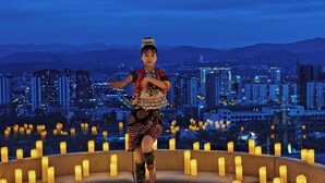 A person performing in a circular area surrounded by candles, with a cityscape in the background.
