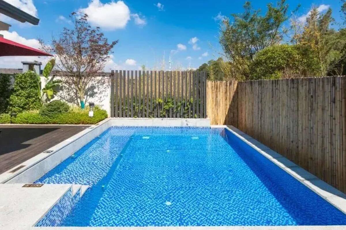 A rectangular swimming pool with a wooden fence and greenery around it.