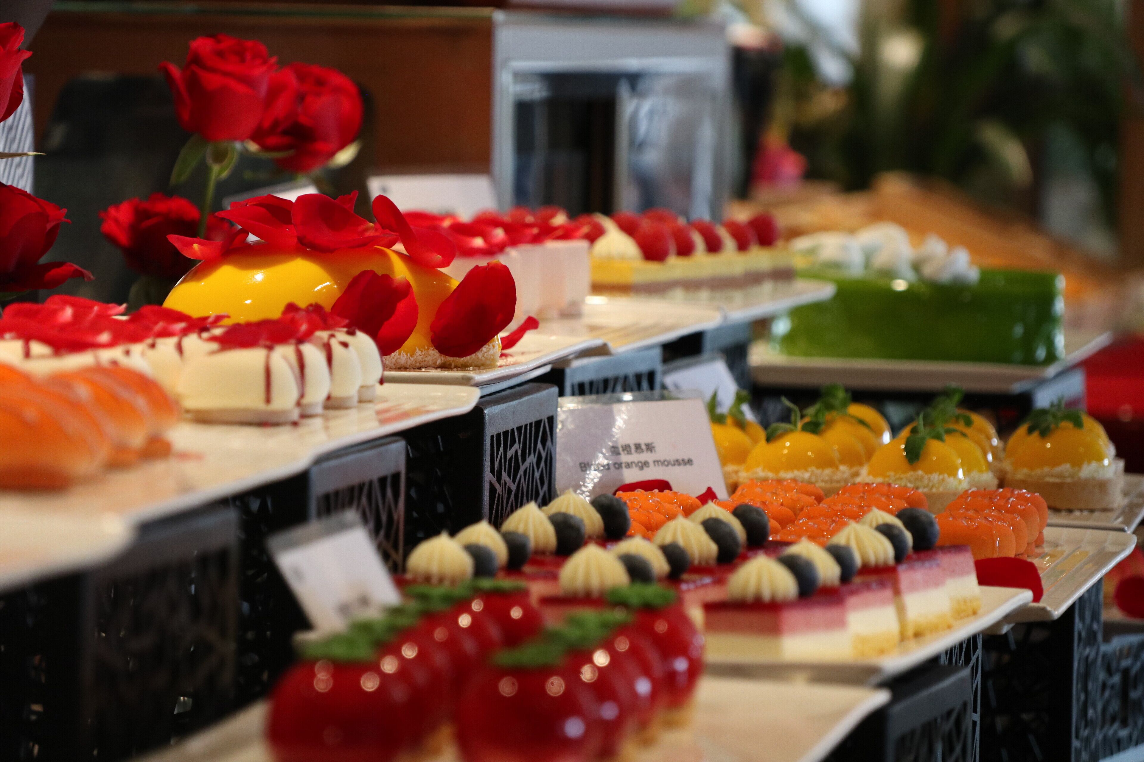 Un espositore di dolci con varie torte e pasticceria, tra cui una torta verde e una torta gialla con una ciliegina sopra.