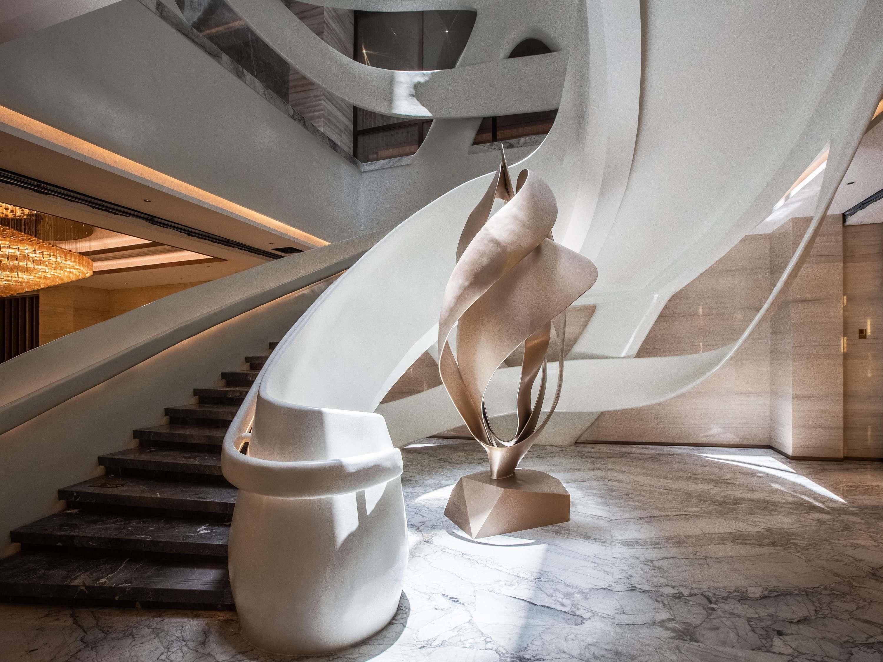 Ein modernes Interieur mit einer geschwungenen Treppe, einer skulpturalen Installation und einem Marmorboden.