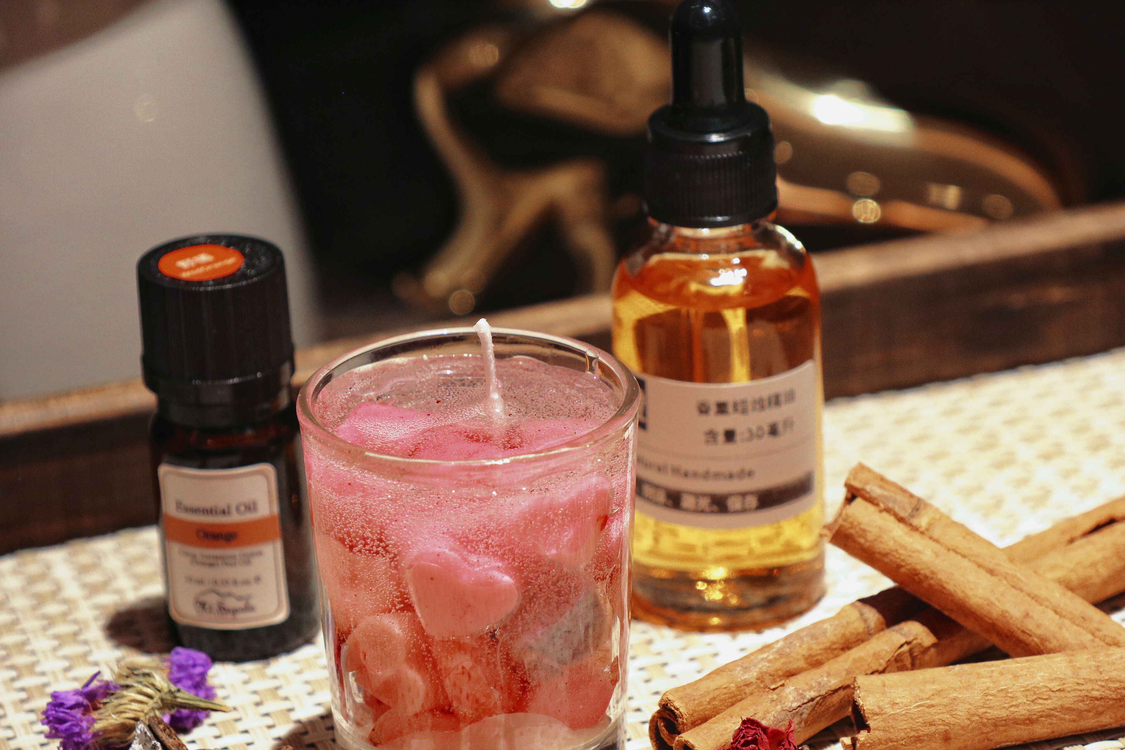 Un vaso con una bebida rosa, una botella de aceite esencial y palitos de canela sobre una mesa.