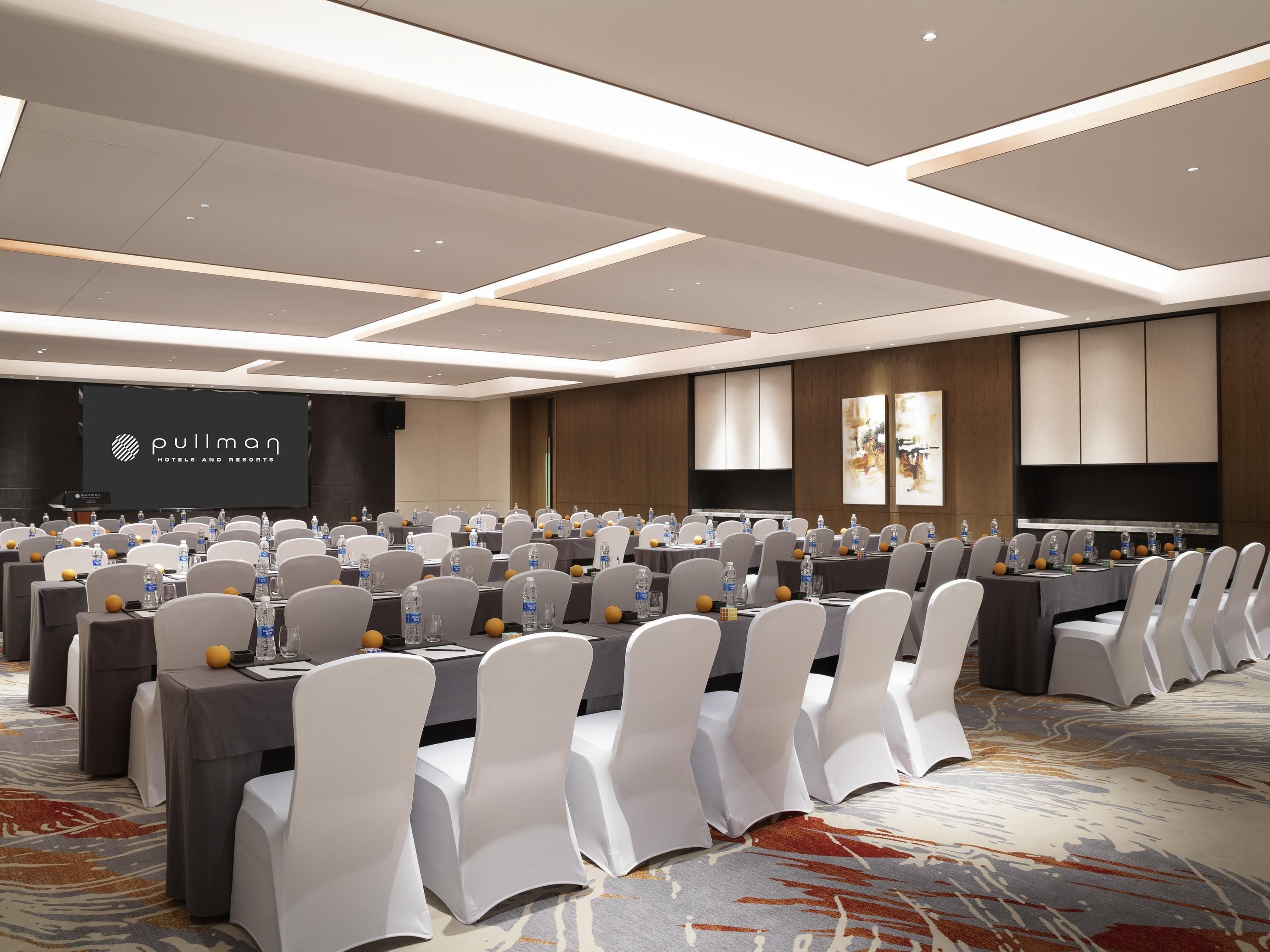 A conference room with tables, chairs, and a large screen displaying the Pullman Hotels and Resorts logo.