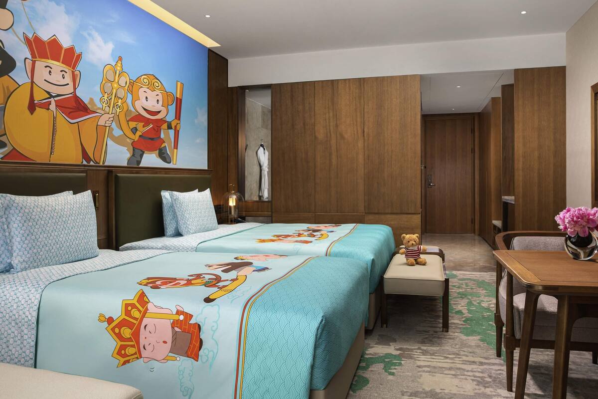 A hotel room with two beds, a dining table, and a mural on the wall.