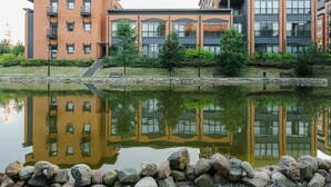 A modern building with a reflection in the water, surrounded by a stone wall and greenery. - Lumina luxury apartment with 3 terraces (Lodz)