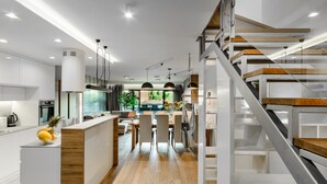A modern kitchen with a central island, wooden flooring, and a staircase with a wooden finish. - Lumina luxury apartment with 3 terraces (Lodz)