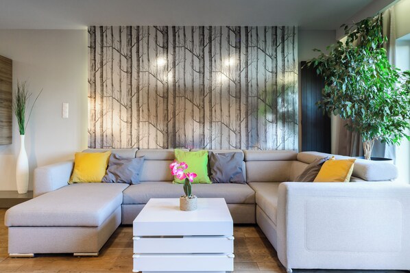 A modern living room with a sectional sofa, a white coffee table, and a wall with a vertical pattern. - Lumina luxury apartment with 3 terraces (Lodz)