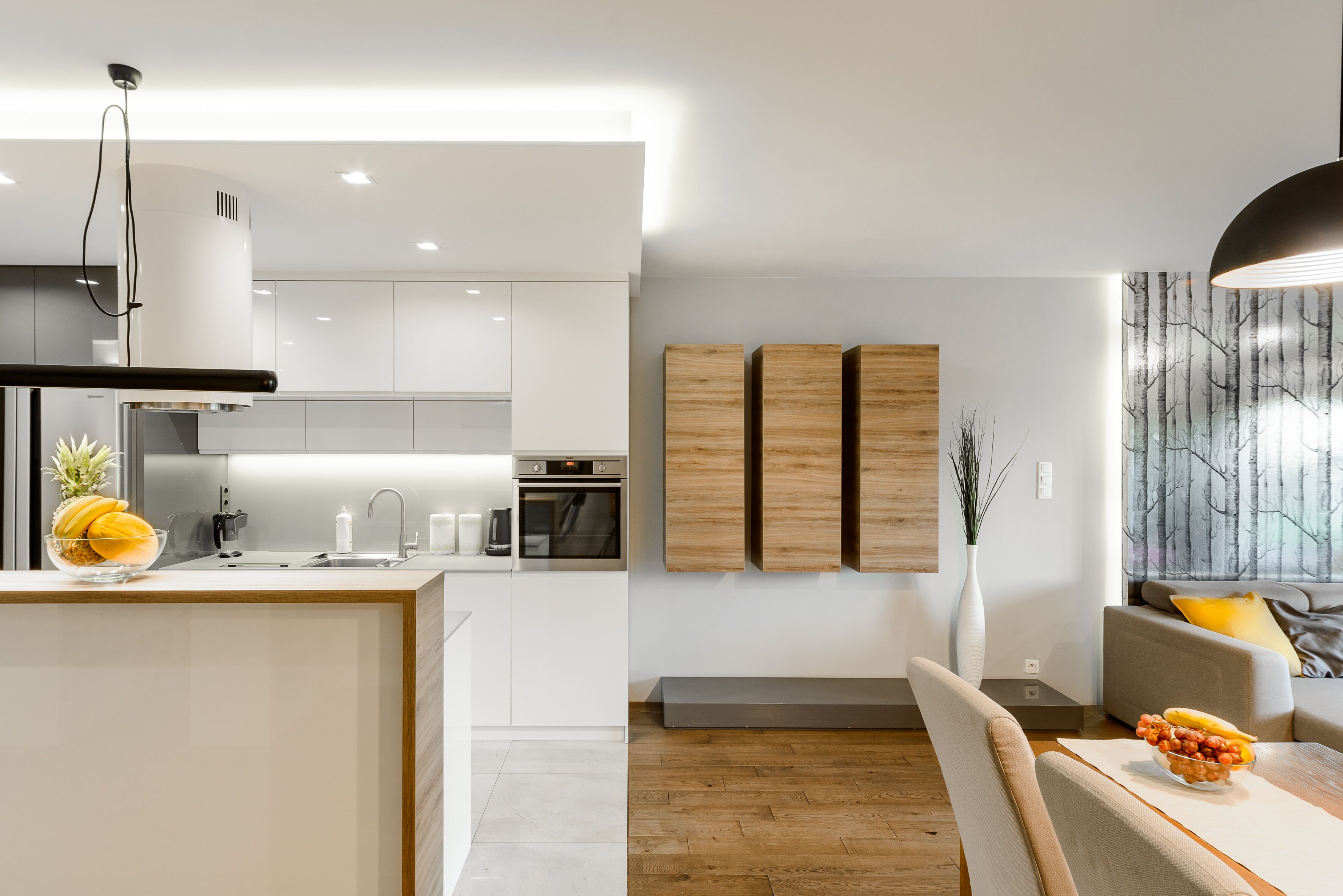 A modern kitchen with white cabinetry, a built-in oven, and a dining area with a wooden table and chairs.