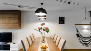 A modern dining area with a wooden table, beige chairs, a vase with flowers, and a hanging chair. - Lumina luxury apartment with 3 terraces (Lodz)