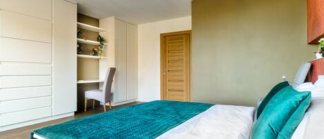 A bedroom with a bed, a teal blanket, a wooden door, and a white wardrobe.