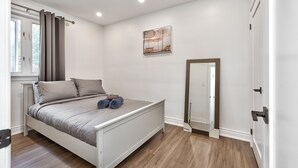 A bedroom with a bed, a window with curtains, a painting on the wall, and a door with a mirror.