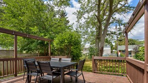 A wooden deck with a table and chairs, surrounded by trees and a fence.