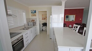 Eine moderne Küche mit weißen Schränken, einem Backofen, einer Mikrowelle und einem Kühlschrank. Es gibt einen Essbereich mit Tisch und Stühlen sowie eine Wand in Rot als Farbakzent.