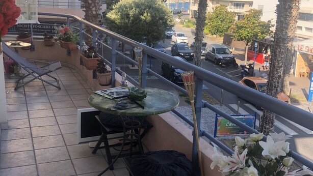 Un balcon avec une table et des chaises, des plantes en pot et une vue sur la rue et les immeubles.