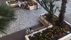 Une place agrémentée de bancs et de parterres de fleurs, une aire de stationnement et un bâtiment avec des panneaux indicateurs.