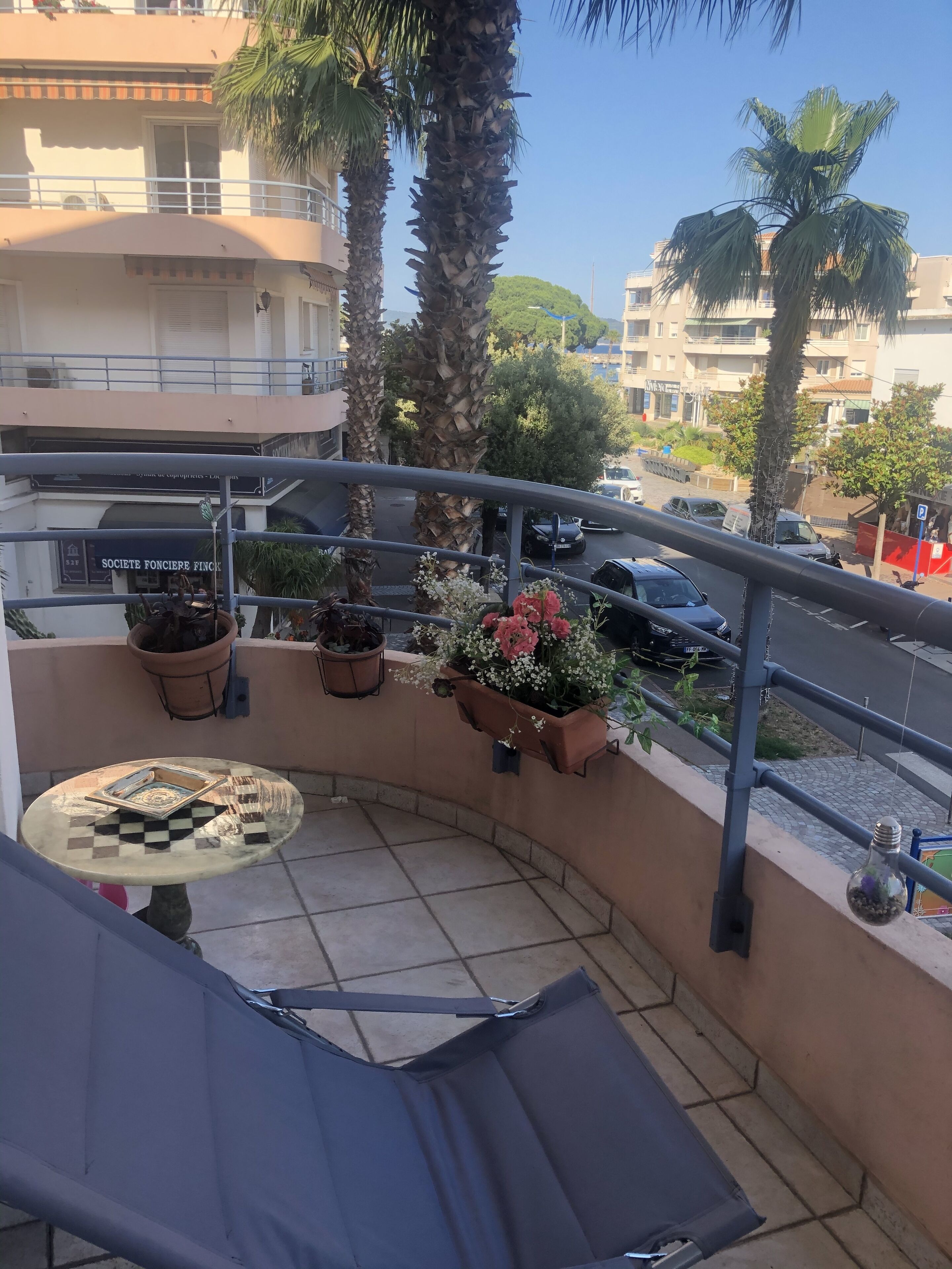 Een balkon met een geruit tafeltje, plantenpotten en uitzicht op de straat.
