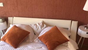 Un lit bien fait, recouvert d’une courtepointe blanche matelassée et agrémenté de deux coussins orange.