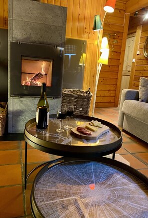 Ein gemütliches Zimmer mit Kamin, Tisch mit einer Weinflasche, Gläsern und einem Käsebrett.