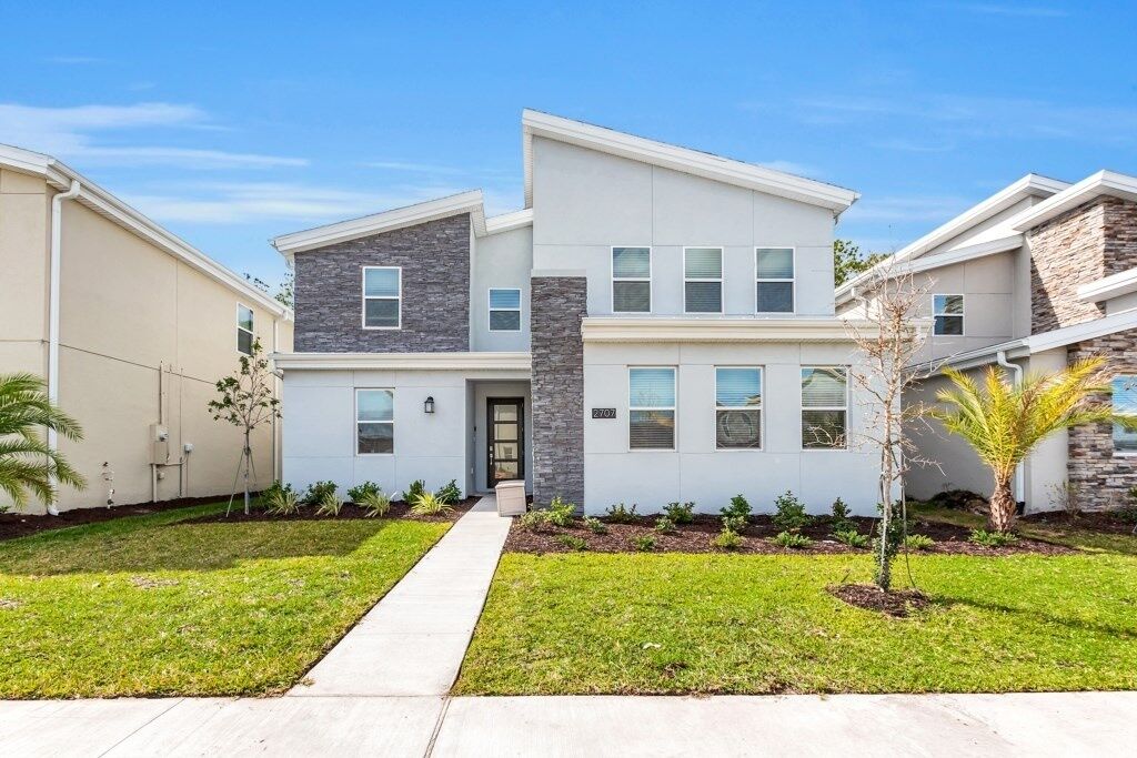 A modern two-story residential building with a stone facade, a central entrance, and a well-maintained lawn.
