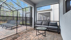 Eine moderne Terrassenanlage im Freien mit Glasverkleidung, einem grauen Sofa und einem Glastisch.