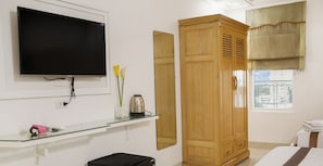 A bedroom with a TV mounted on the wall, a wooden wardrobe, a bedside table with a kettle, and a window with a view. - Caroline Beach Vung Tau (Ho Chi Minh City)