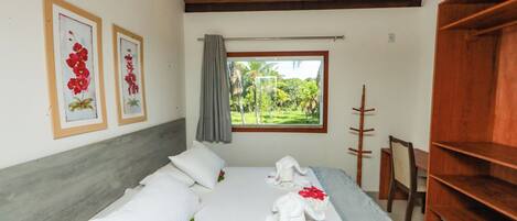 Una habitación de hotel con una cama, cabecera de madera, ventana con vistas a zonas verdes y una estantería de madera.