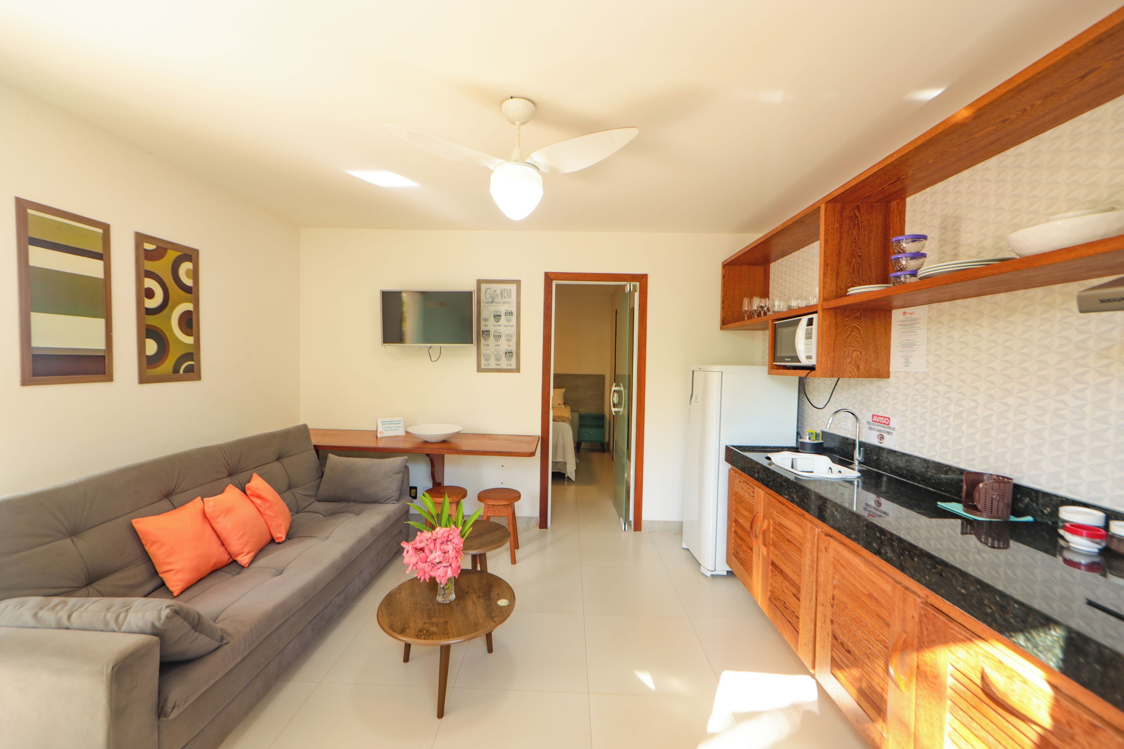 A modern living room with a sofa, coffee table, and a TV. There is a kitchen area with a microwave, sink, and cabinets.