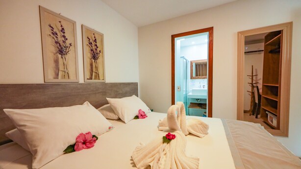 Ein ordentlich bezogenes Bett mit Handtüchern und einer Blume, ein Holz-Kopfteil und ein Spiegel darüber.