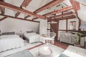 Un dormitorio con dos camas, una silla colgante, un aparador y una planta grande.