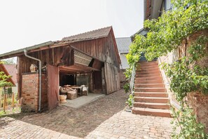 Un edificio de madera rústico con una chimenea de ladrillo, un área de estar al aire libre techada y una escalera de piedra que conduce a la entrada del segundo piso.