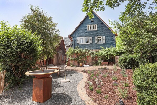 Una casa azul con techo inclinado, rodeada de un jardín con senderos de grava y diversas plantas.
