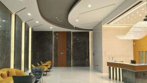 Un hall d’hôtel moderne comprenant un comptoir d’accueil, un espace salon avec des fauteuils et un luminaire décoratif.