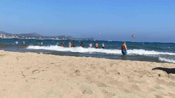 A beach with people swimming and walking along the shore.