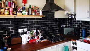 A kitchen with black tiled backsplash, a gas stove, a kettle, and various kitchen items on shelves. - Appartement 100m2 Dernier Étage Calme et Lumineux (Melun)